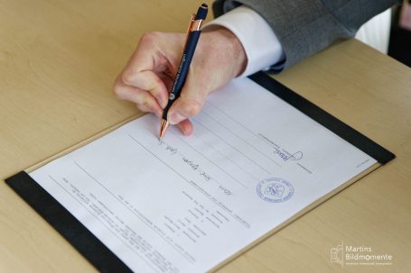 Eine Hand schreibt mit einem Stift auf ein Dokument mit einem offiziellen Stempel.