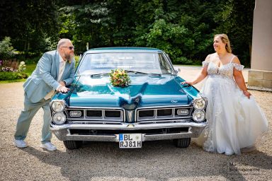 Paar in Hochzeitskleidung, posierend neben einem vintage Auto mit Blumenarrangement.