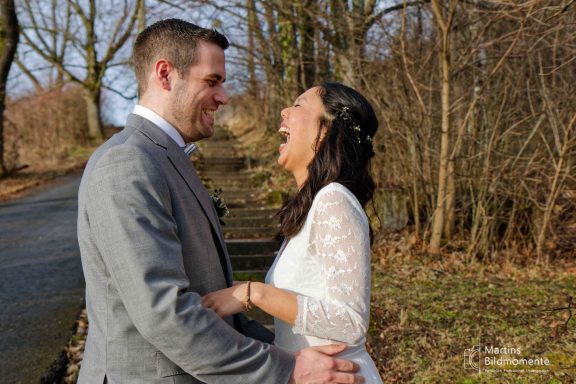 Ein Paar lacht freudig im Freien, umgeben von Bäumen und natürlichem Licht.