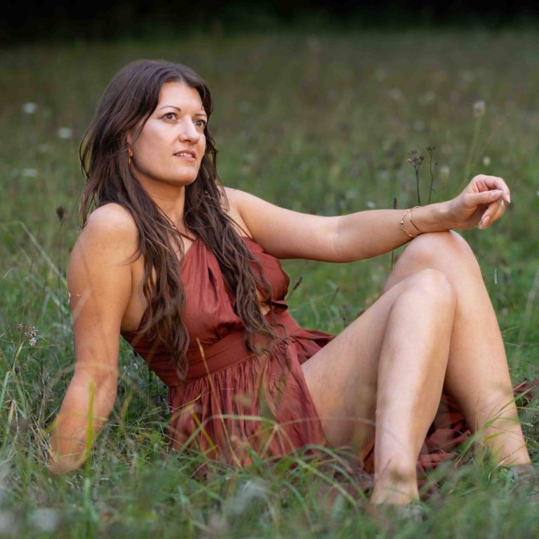 Frau in einem roten Kleid, entspannt auf einer Wiese sitzend.