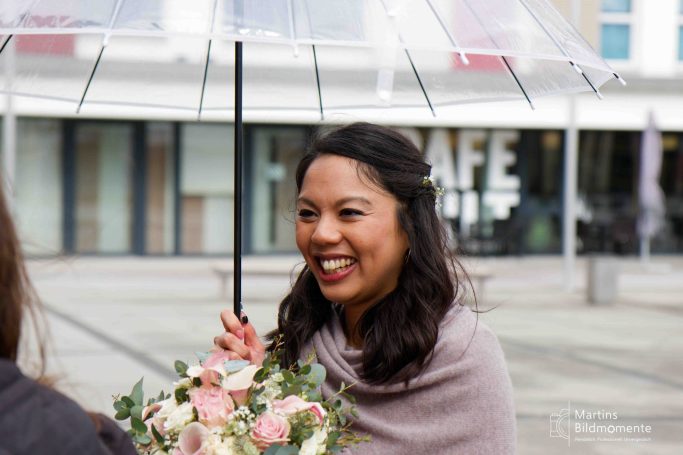 Frau mit einem Regenschirm, lächelnd und einen Blumenstrauß haltend.