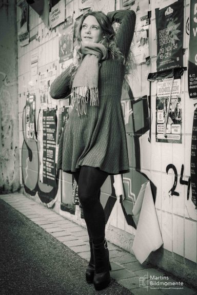 Frau in einem grünen Kleid und Schal posiert vor einer Graffiti-Wand.