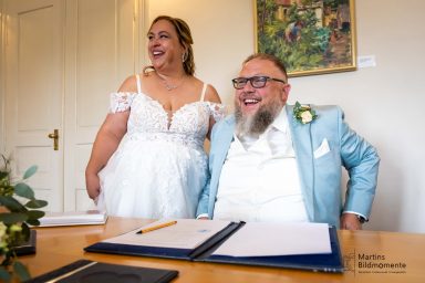 Braut und Bräutigam lächeln glücklich am Hochzeitstisch, festlich gekleidet.