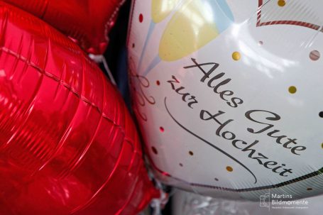 Rote Herzluftballons und ein weißer Ballon mit der Aufschrift "Alles Gute zur Hochzeit".