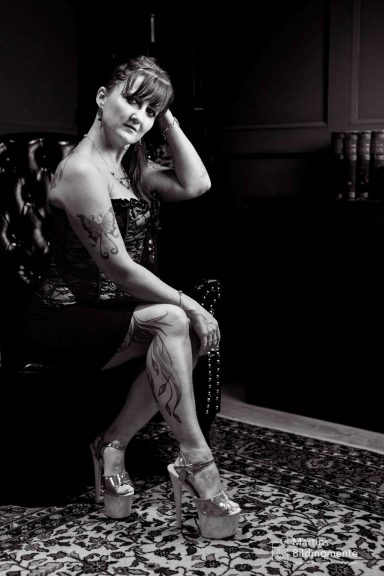 Frau mit Tattoos sitzt in einem eleganten Outfit auf einem Stuhl.