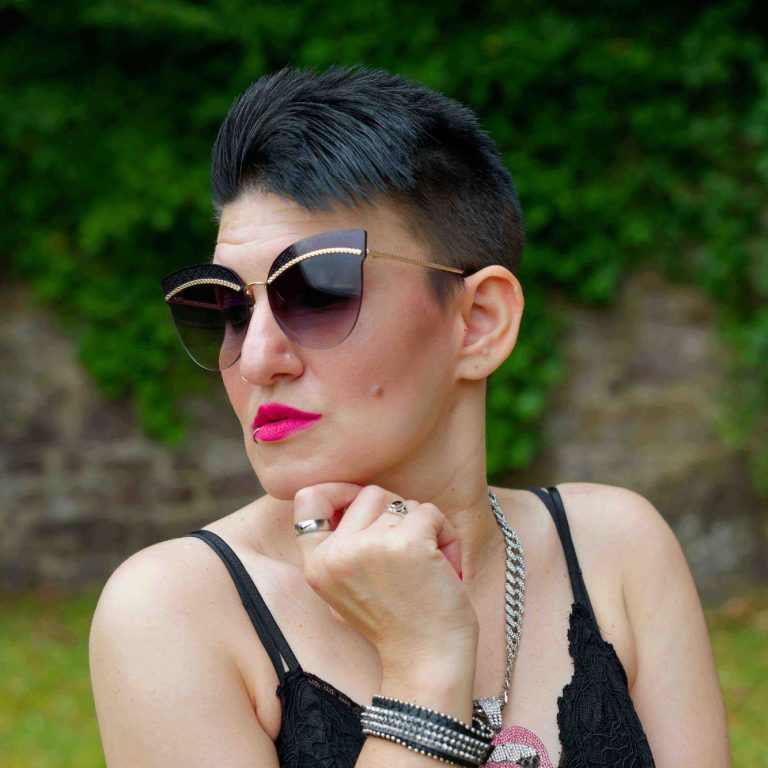 Frau mit kurzen Haaren, Sonnenbrille und auffälligem Make-up im Freien.