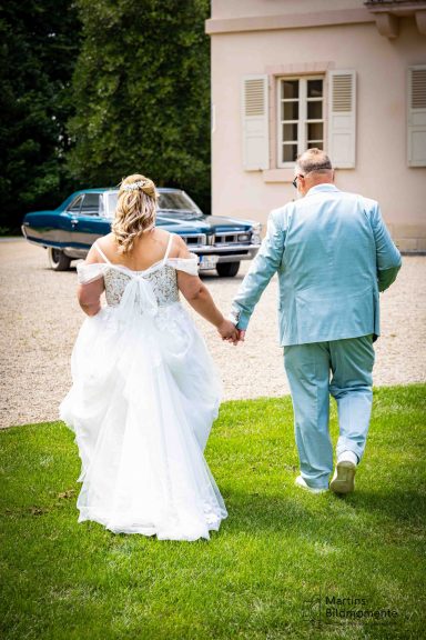 Braut und Bräutigam halten Händchen und gehen in Richtung eines Autos.